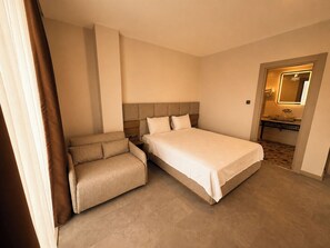 Una habitación de hotel con cama, sofá, baño con espejo y piso de baldosas.