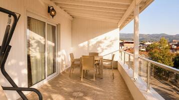 A balcony with a table and chairs, a glass door, and a view of the surrounding landscape.