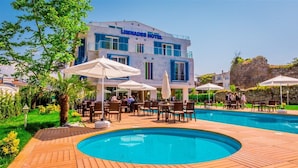 Zona de piscina con mobiliario exterior y un edificio que dice "LIMNADES HOTEL".