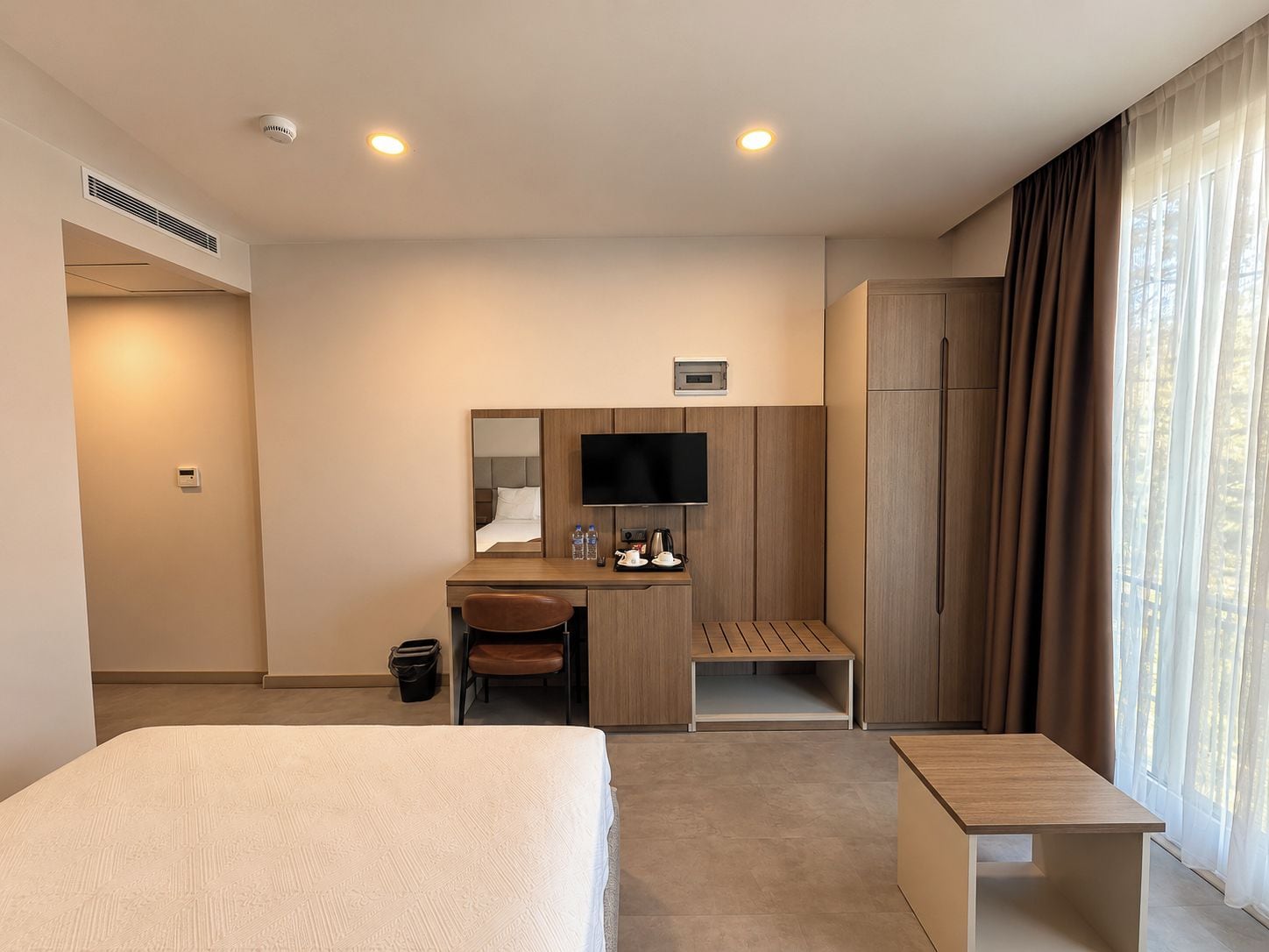 A hotel room with a bed, desk, chair, television, and a window with curtains.