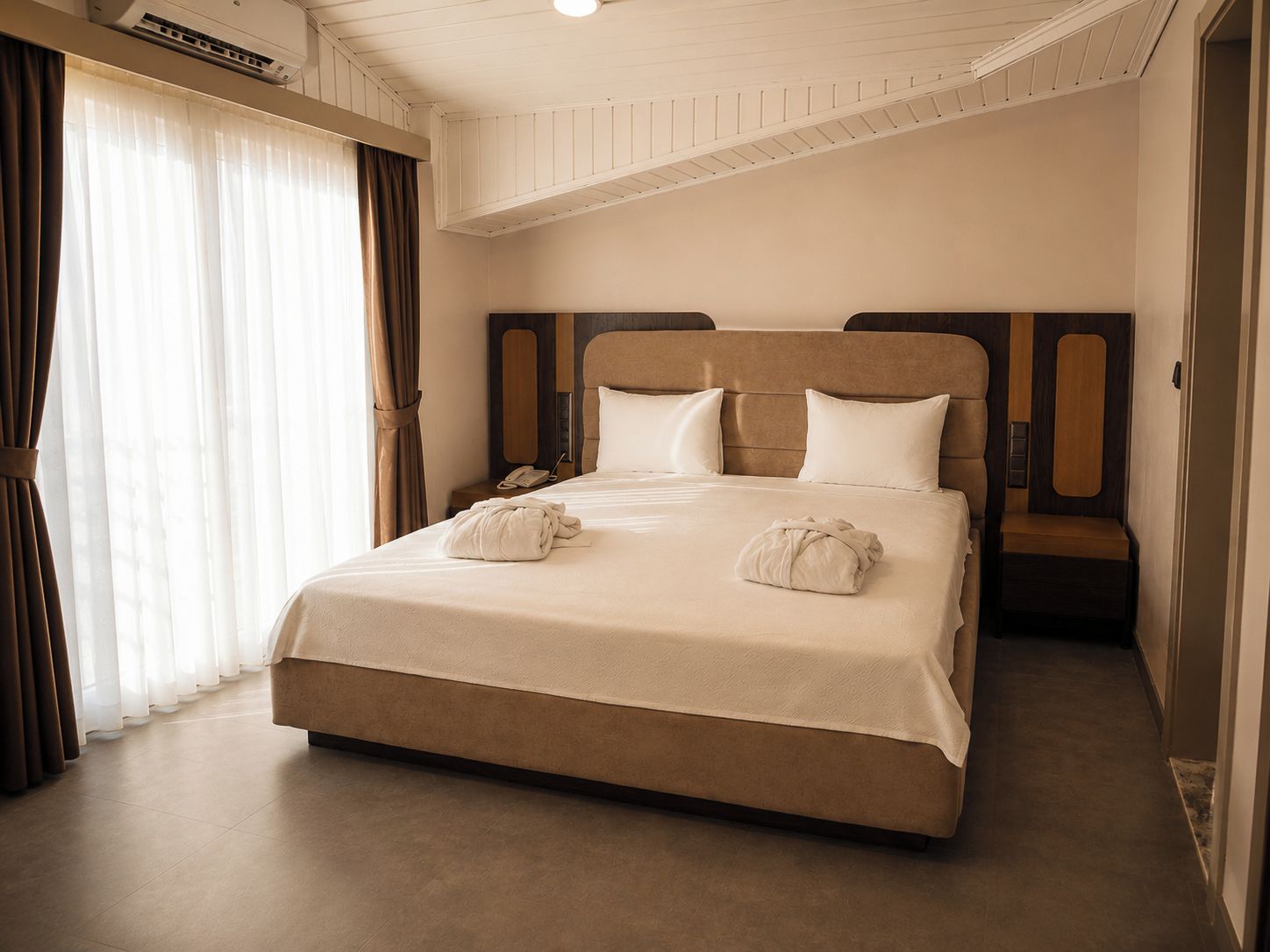 Una habitación de hotel con una cama, una mesita de noche, un teléfono y una ventana con cortinas.