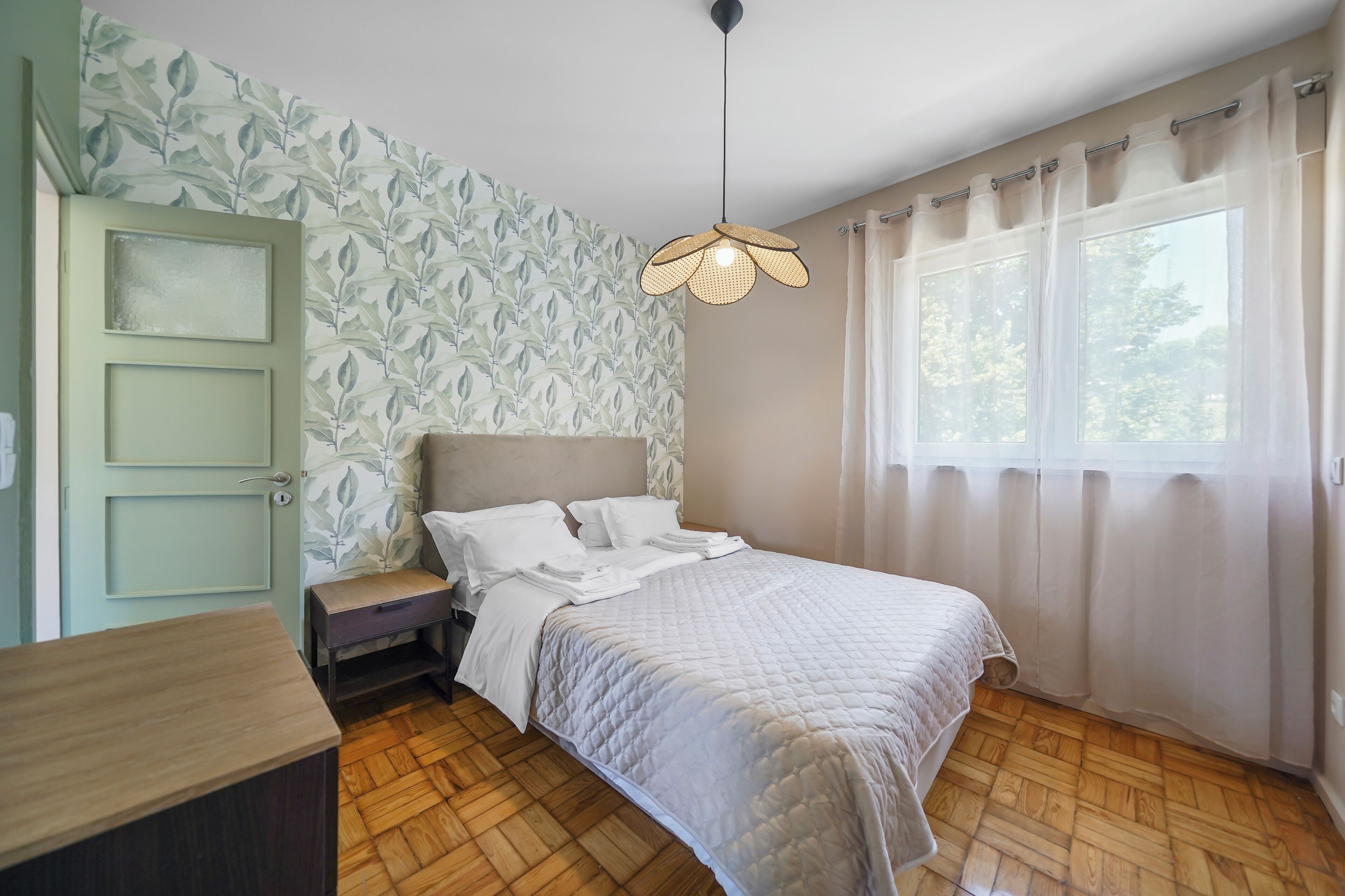 A bedroom with a bed, bedside table, and a window with curtains.