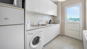 A compact kitchen with a washing machine, a microwave, and a sink. - Apartments Luiz I Bridge (Vila Nova de Gaia)