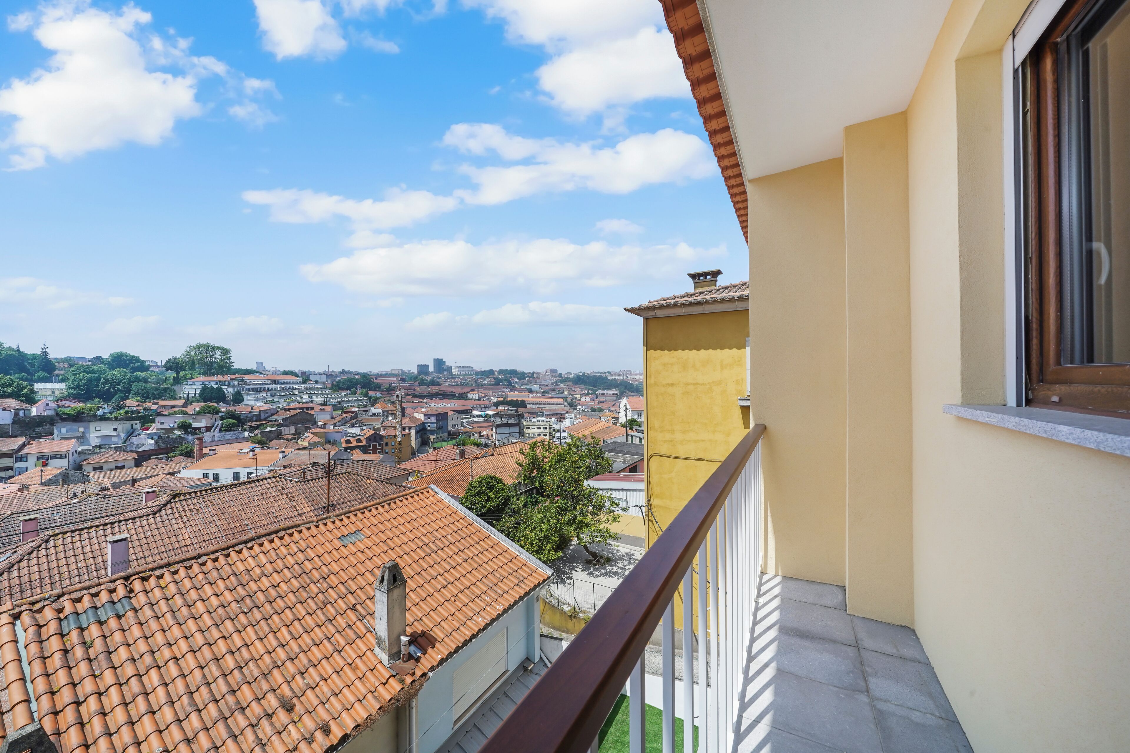 A balcony with a view of a cityscape, featuring terracotta rooftops and a clear sky.
