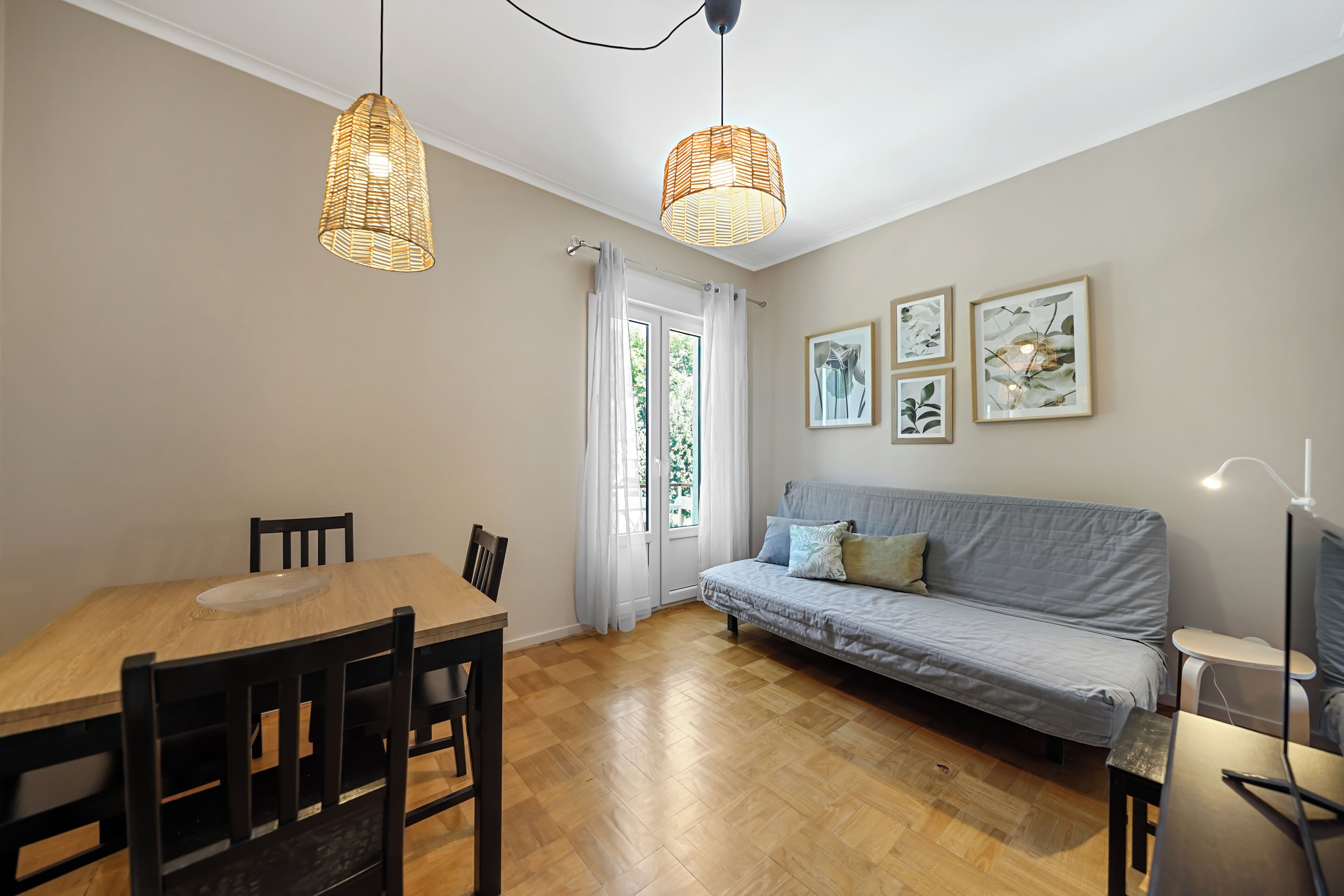 Een eetgedeelte met een houten tafel en stoelen, een grijze bank en twee rieten hanglampen.