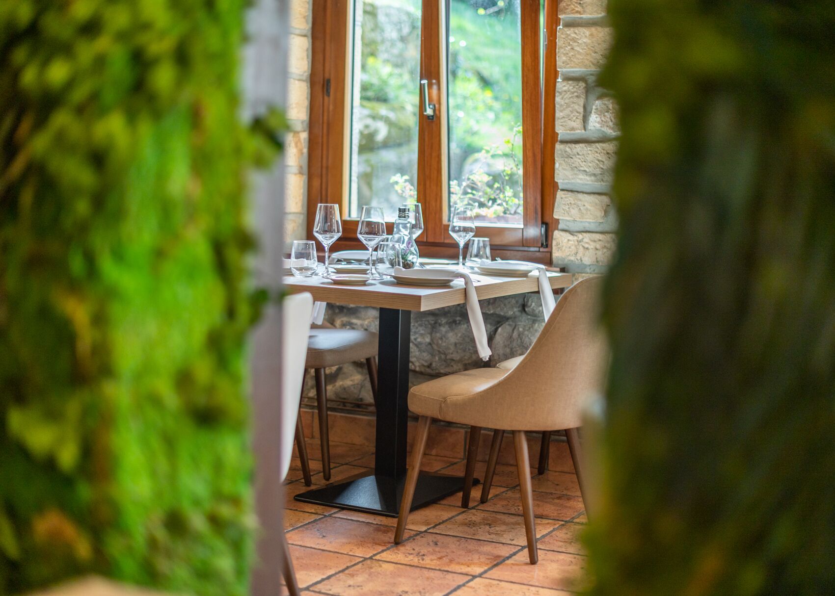 A dining table set with wine glasses and plates, a chair, and a stone wall in the background.