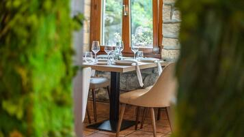 A dining table set with wine glasses and plates, a chair, and a stone wall in the background.