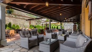 An outdoor patio with wicker furniture, stone flooring, and a stone wall backdrop. - Logis Hotel Restaurante La Casa de Juansabeli (Cabrales)