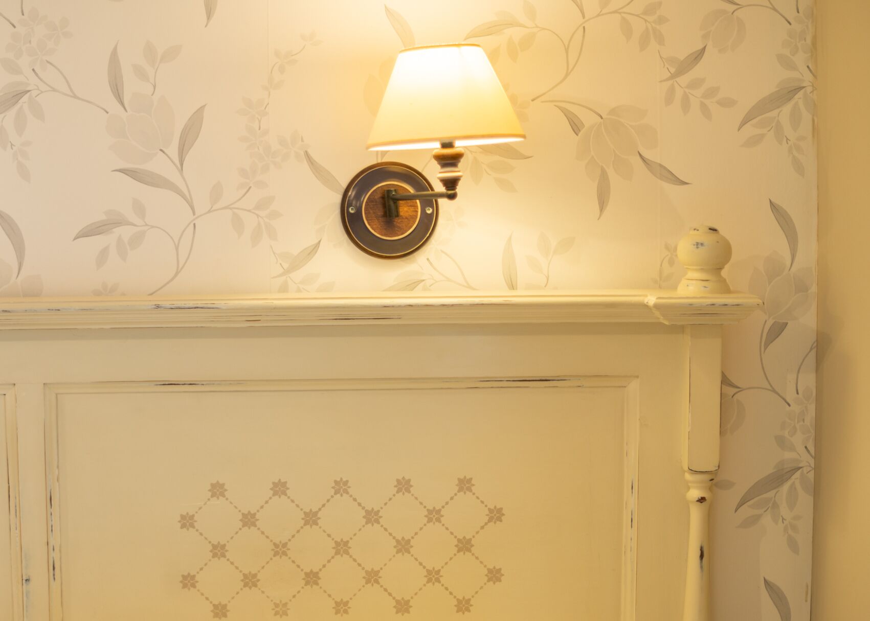 A wall-mounted lamp with a floral wallpaper pattern and a decorative fireplace with a diamond-patterned door.