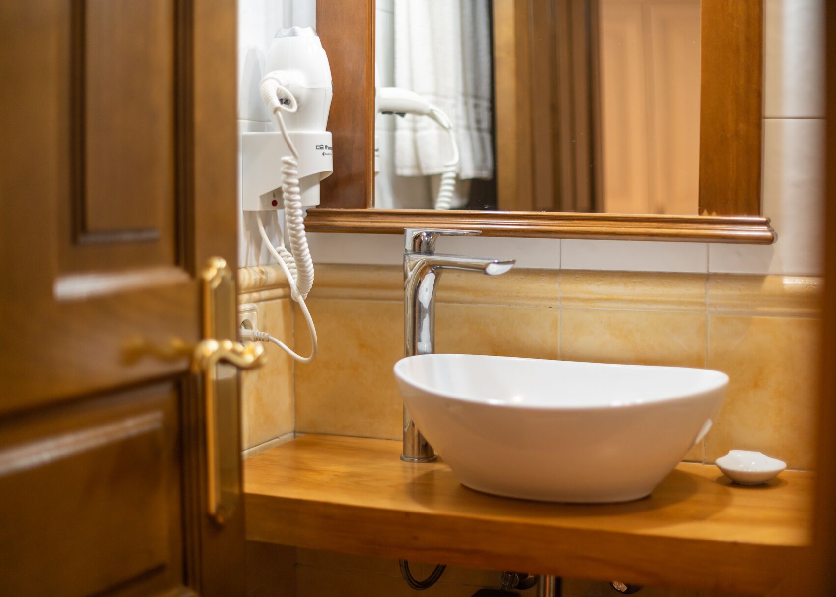 A bathroom with a white sink, a mirror, and a hairdryer on a wall-mounted stand.