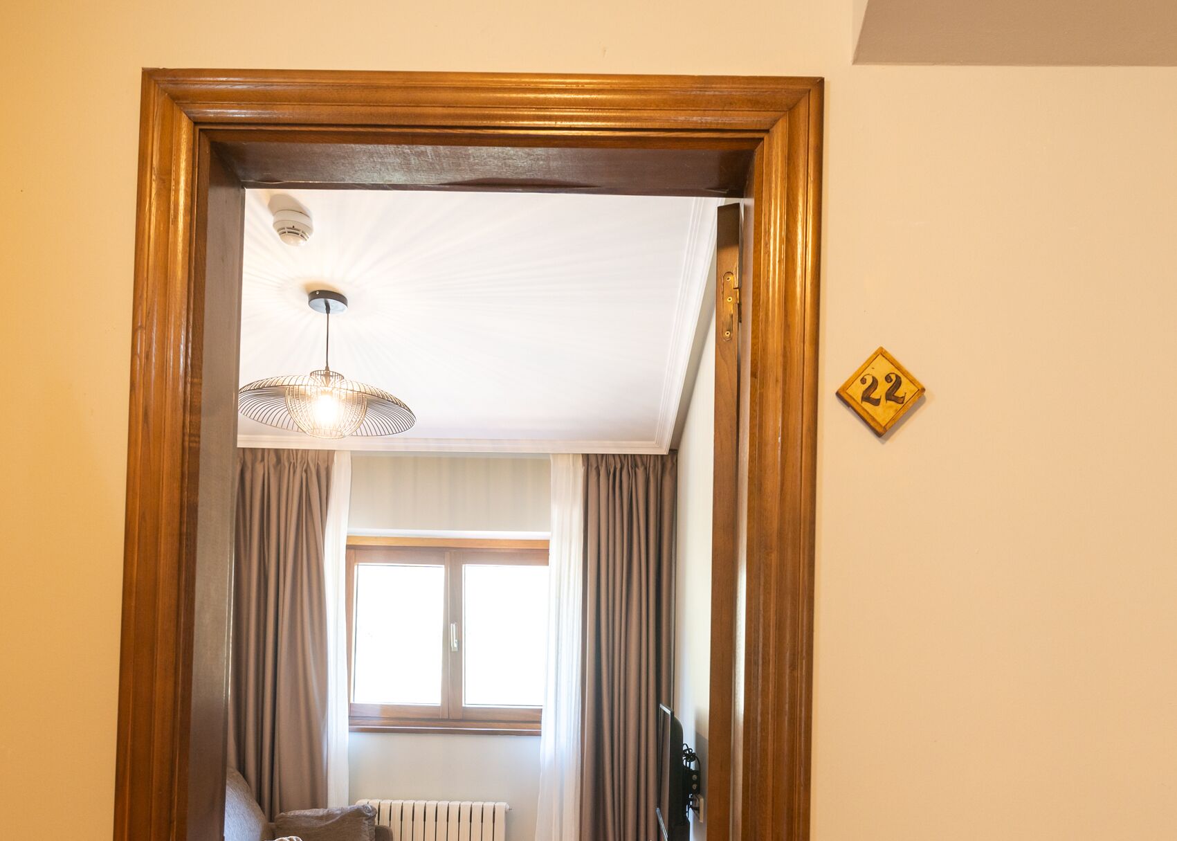 A room with a wooden-framed doorway, a hanging light fixture, a window with curtains, and a radiator.