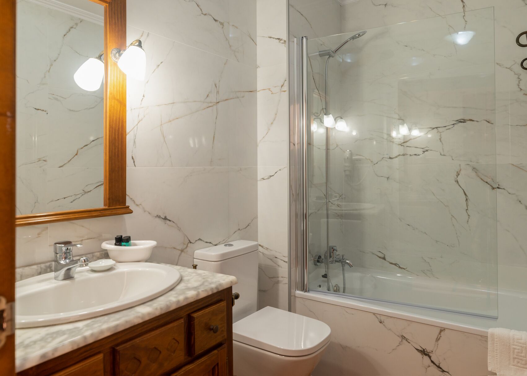 Ein Badezimmer mit Marmorwaschbecken, einer Glaskabine für die Dusche und einer Toilette.