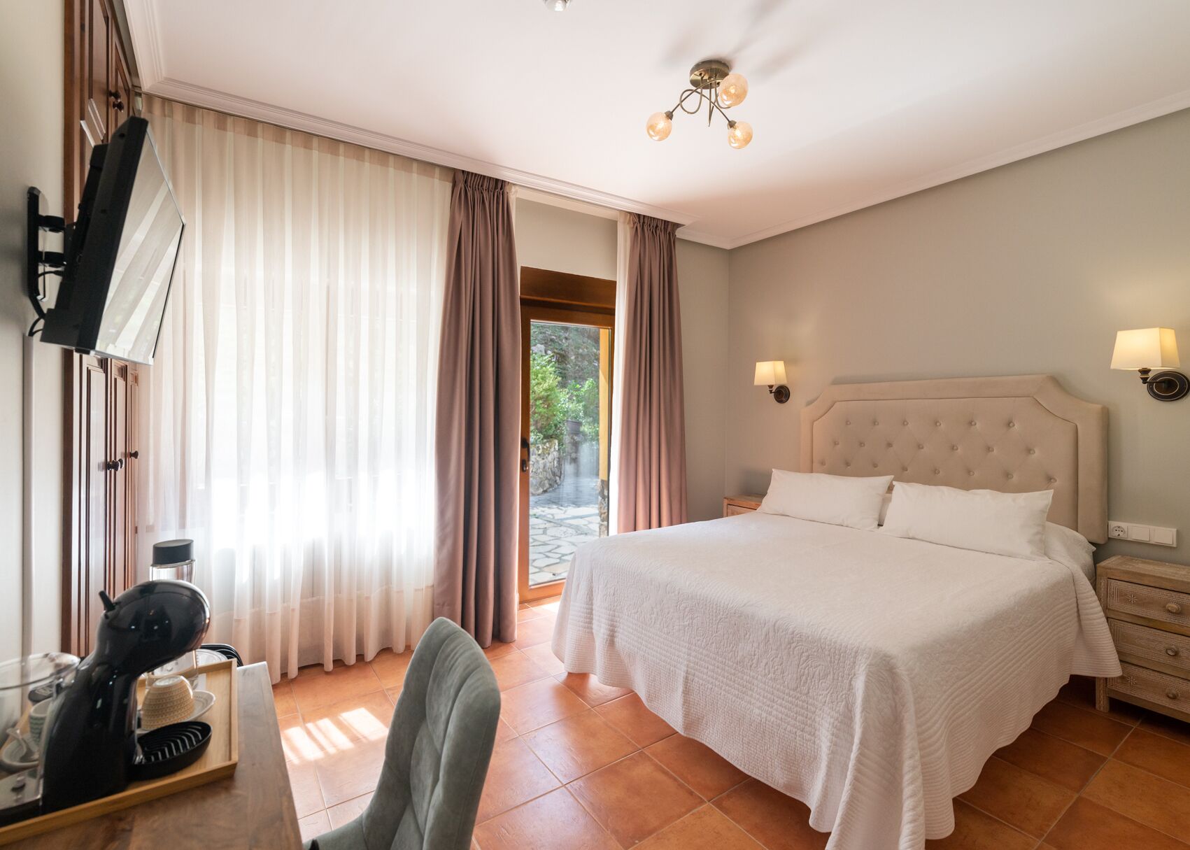 Habitació d'hotel amb un llit gran, una taula amb assecador, una cadira i un televisor.