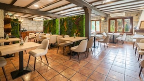 A restaurant with exposed wooden beams, stone walls, and green vertical gardens. Tables and chairs are arranged for dining. - Logis Hotel Restaurante La Casa de Juansabeli (Cabrales)