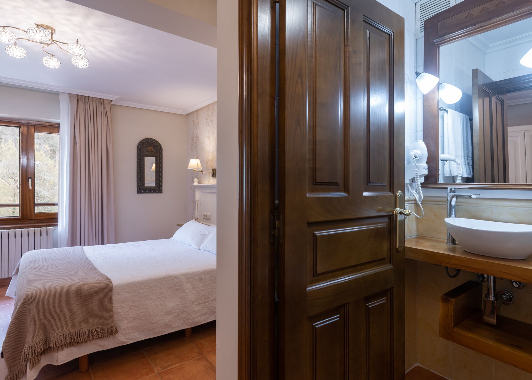 Una habitación de hotel con una cama, una puerta de madera, y un baño con lavabo y espejo.