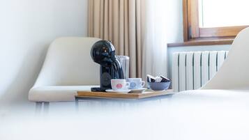Una habitación de hotel moderna con una elegante cafetera negra sobre una bandeja, un sofá blanco y una ventana con cortinas.