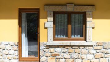 Un muro de piedra con una puerta de madera y una ventana con cortinas.