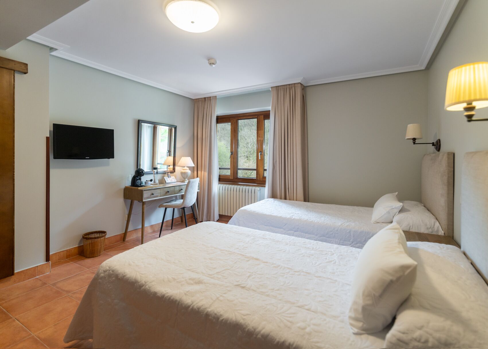 Een hotelkamer met twee bedden, een bureau, een televisie en een raam met gordijnen.