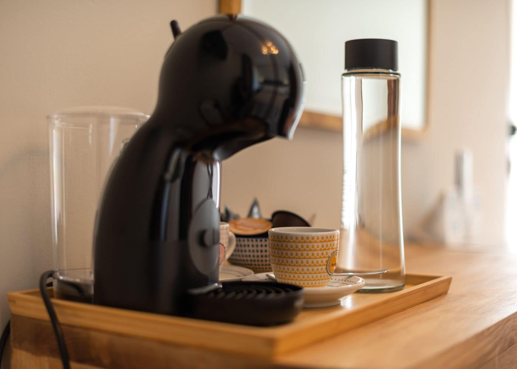Un secador negro sobre una bandeja de madera, junto a un recipiente de vidrio y tazas decoradas.