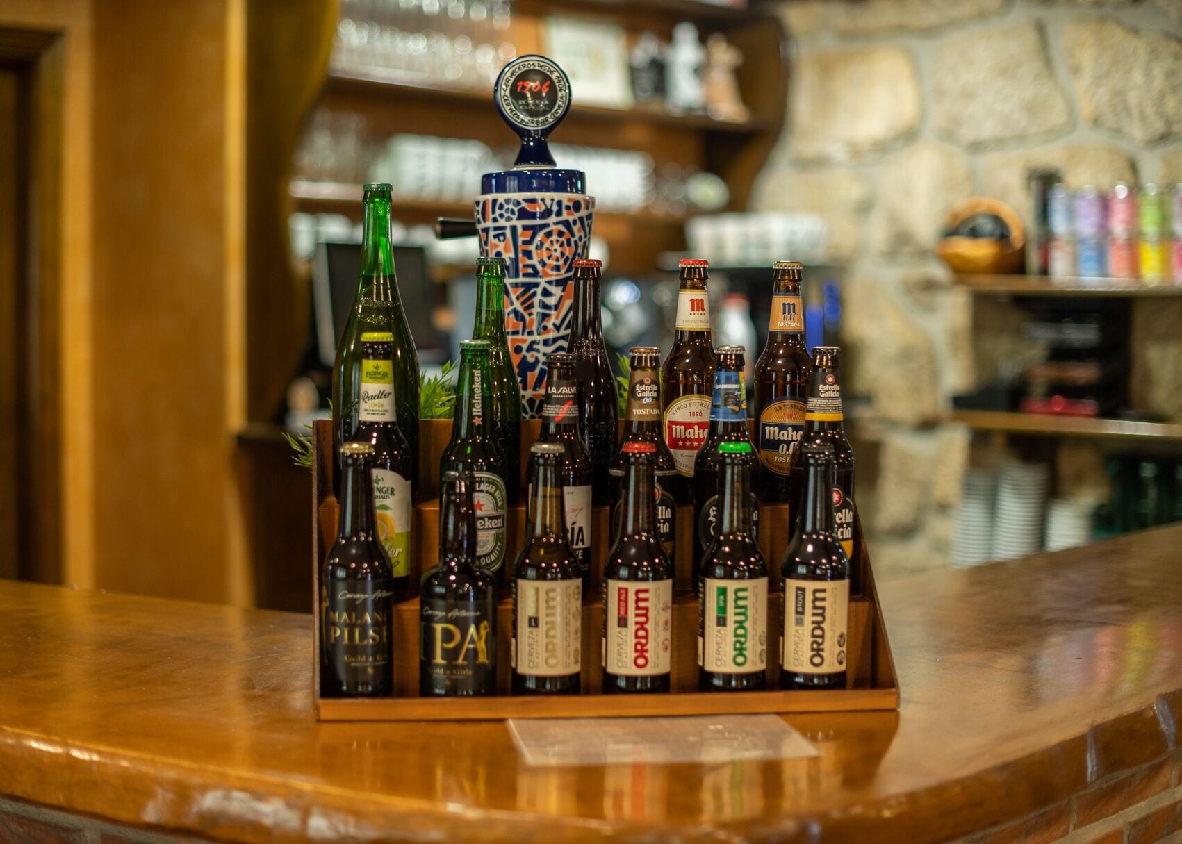 Un comptoir de bar où sont exposées différentes bouteilles, dont des marques comme Heineken et Malani Pilsner, ainsi qu’une chope décorative au motif rétro.