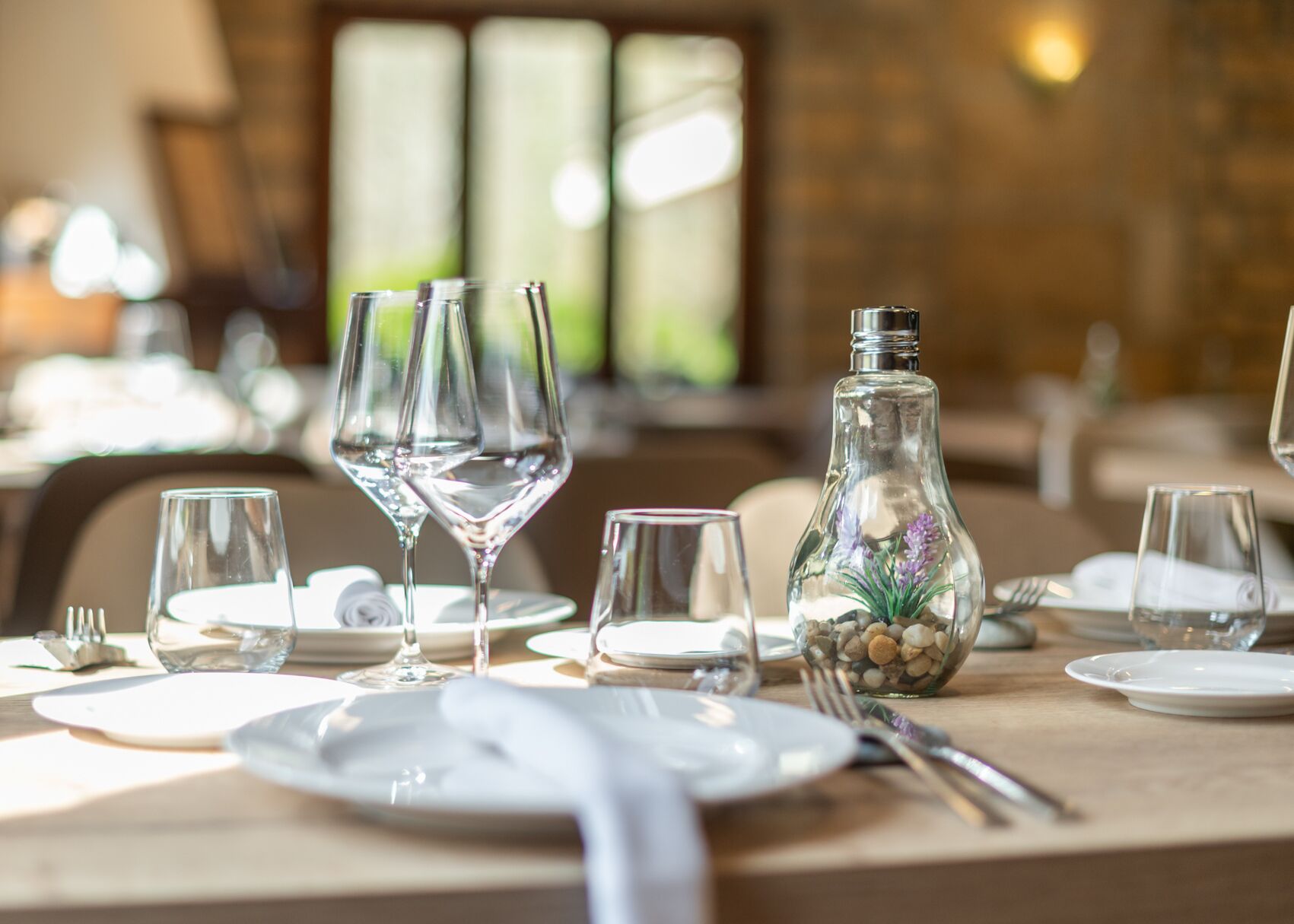 Una tavola imbandita con diversi bicchieri da vino, una bottiglia di vetro decorativa e vari utensili da tavola.
