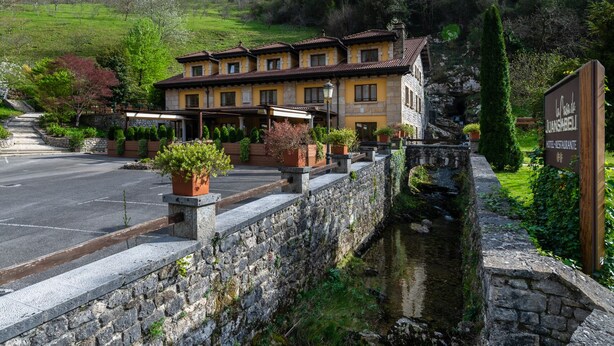A traditional stone building with a courtyard, a small canal, and a sign indicating it is a hotel and restaurant. - Logis Hotel Restaurante La Casa de Juansabeli (Cabrales)