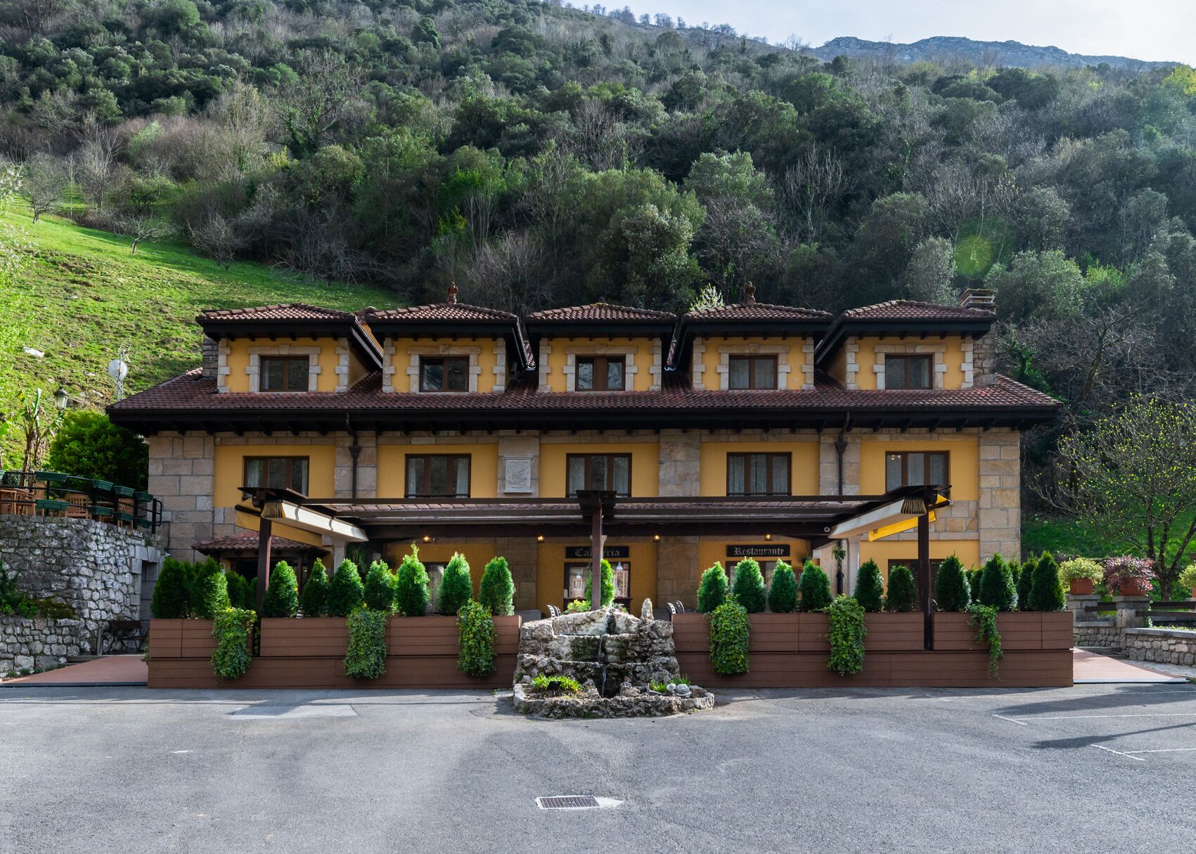 A hotel with a traditional architectural style, featuring a central courtyard with a fountain, surrounded by neatly trimmed hedges and potted plants.
