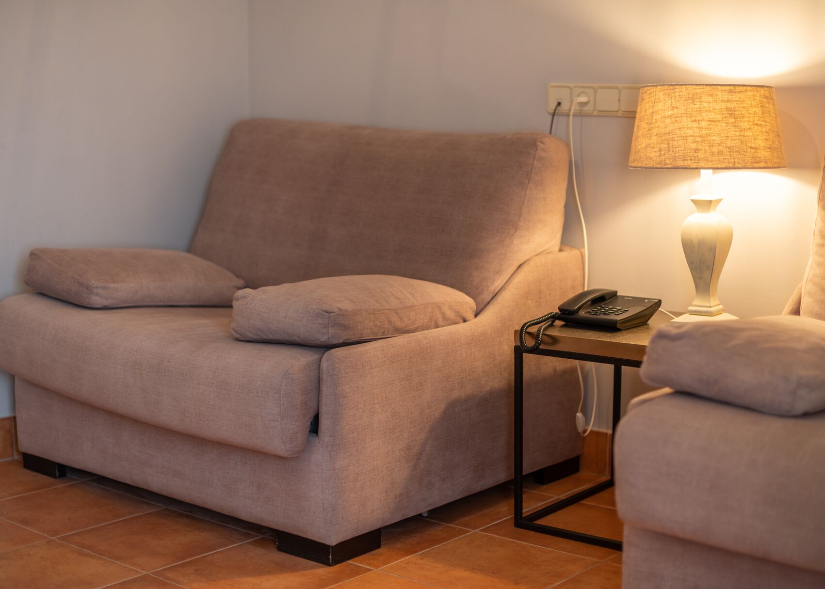 En beige fåtölj med ett sidobord, en lampa och en telefon.