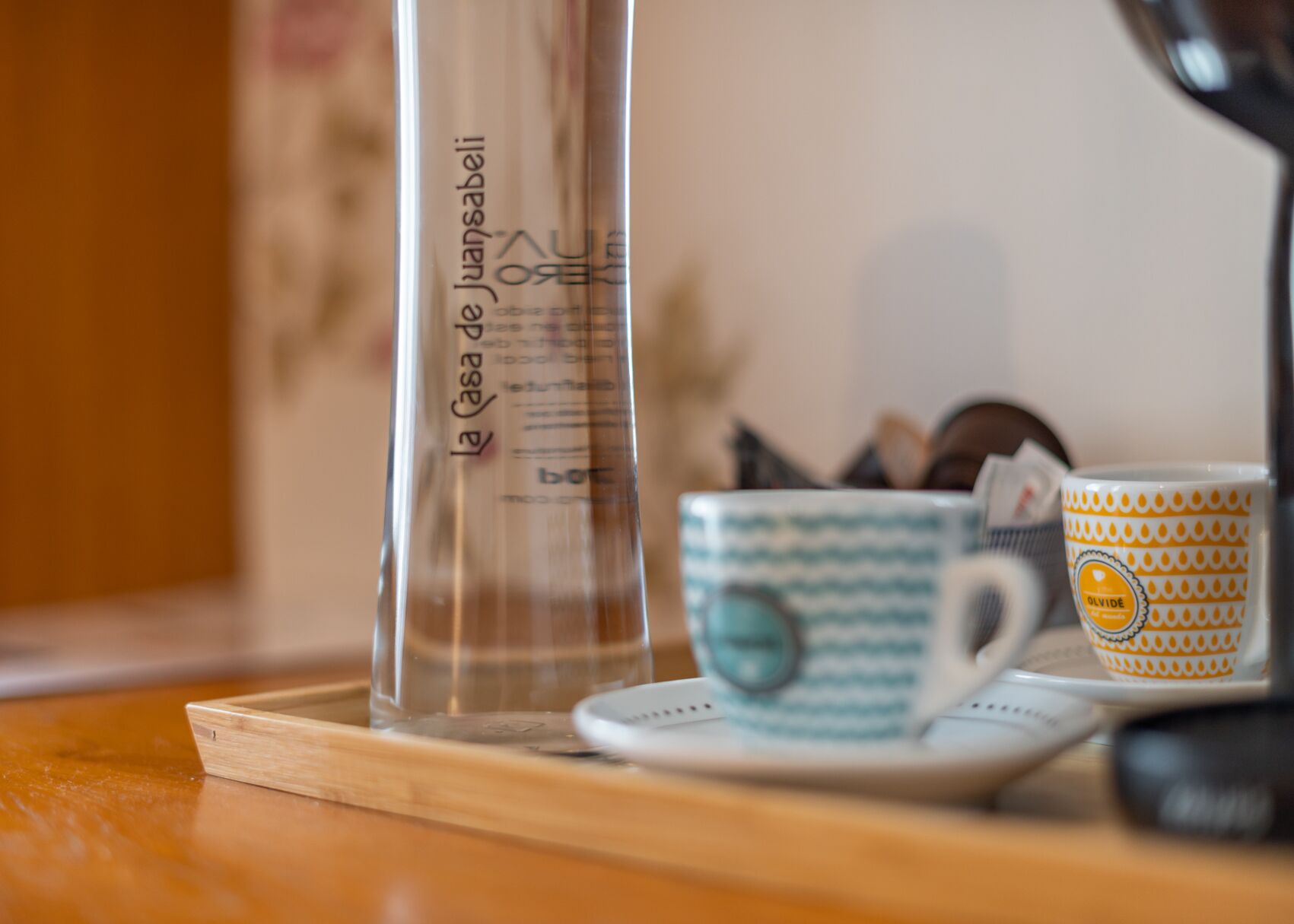 Une bouteille en verre transparent avec du texte, une tasse en céramique ornée d’un motif bleu et un plateau en bois.