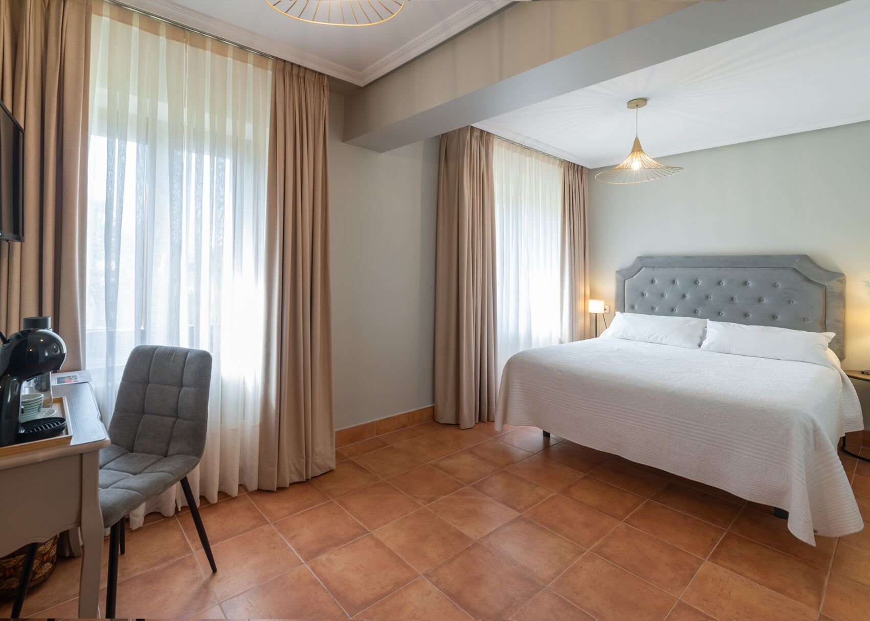 A hotel room with a bed, a chair, a desk with a coffee maker, and a lamp.