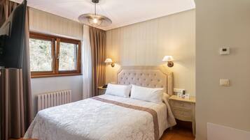 A bedroom with a large bed, a window, a radiator, a wall-mounted light, and a thermostat.