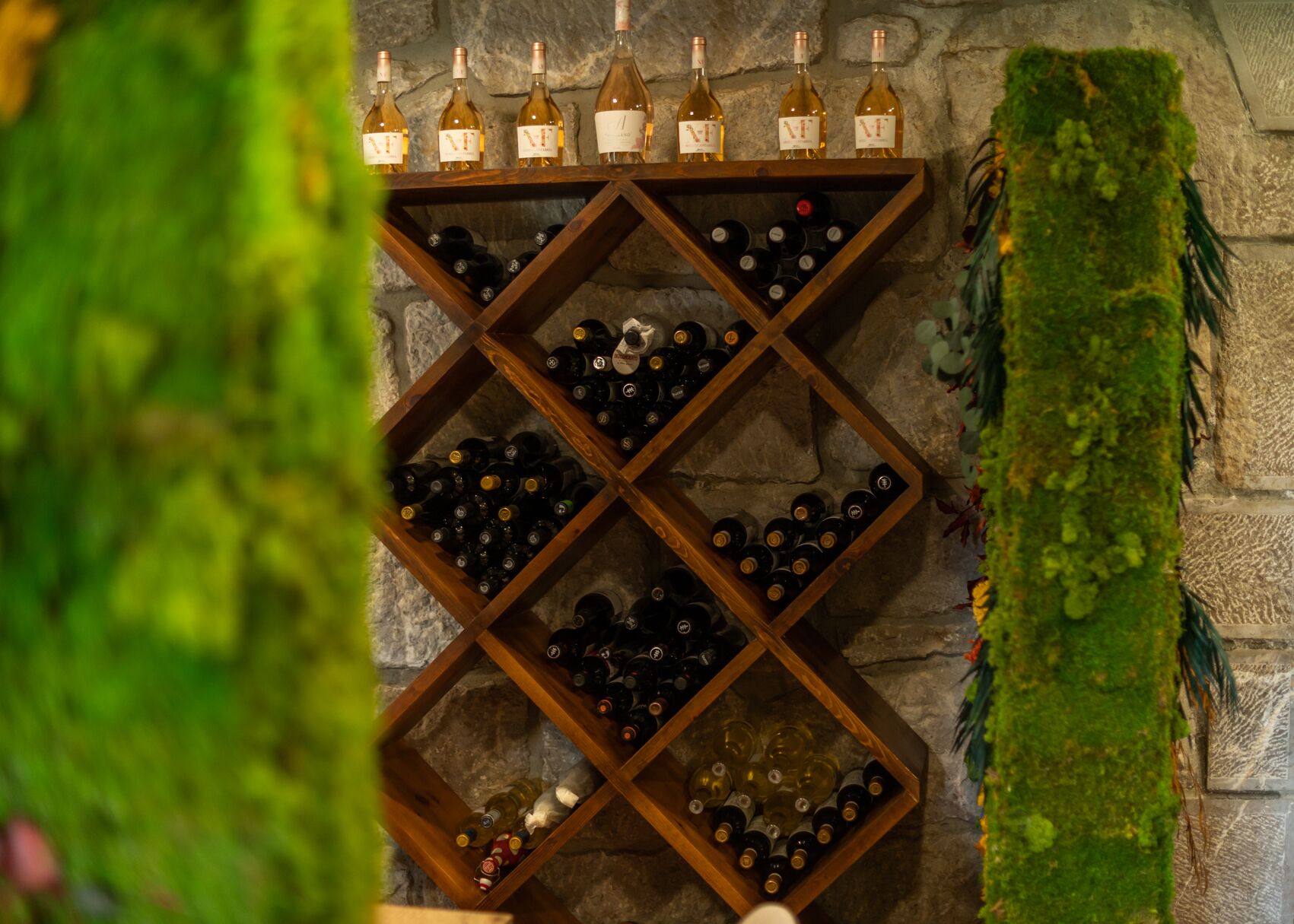 Una estantería con botellas de vino frente a una pared de piedra.