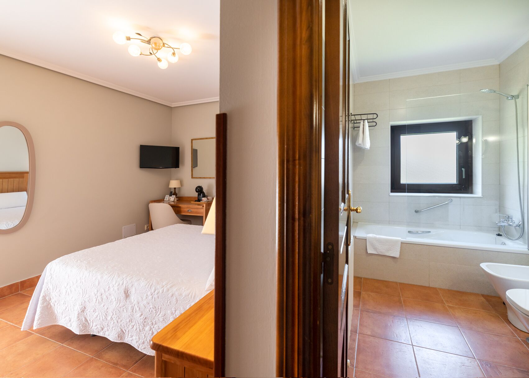 Ein Hotelzimmer mit Bett, Schreibtisch mit Lampe, Fernseher und einem Badezimmer mit Badewanne und Waschbecken.