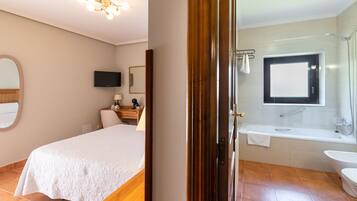 Ein Hotelzimmer mit Bett, Schreibtisch mit Lampe, Fernseher und einem Badezimmer mit Badewanne und Waschbecken.