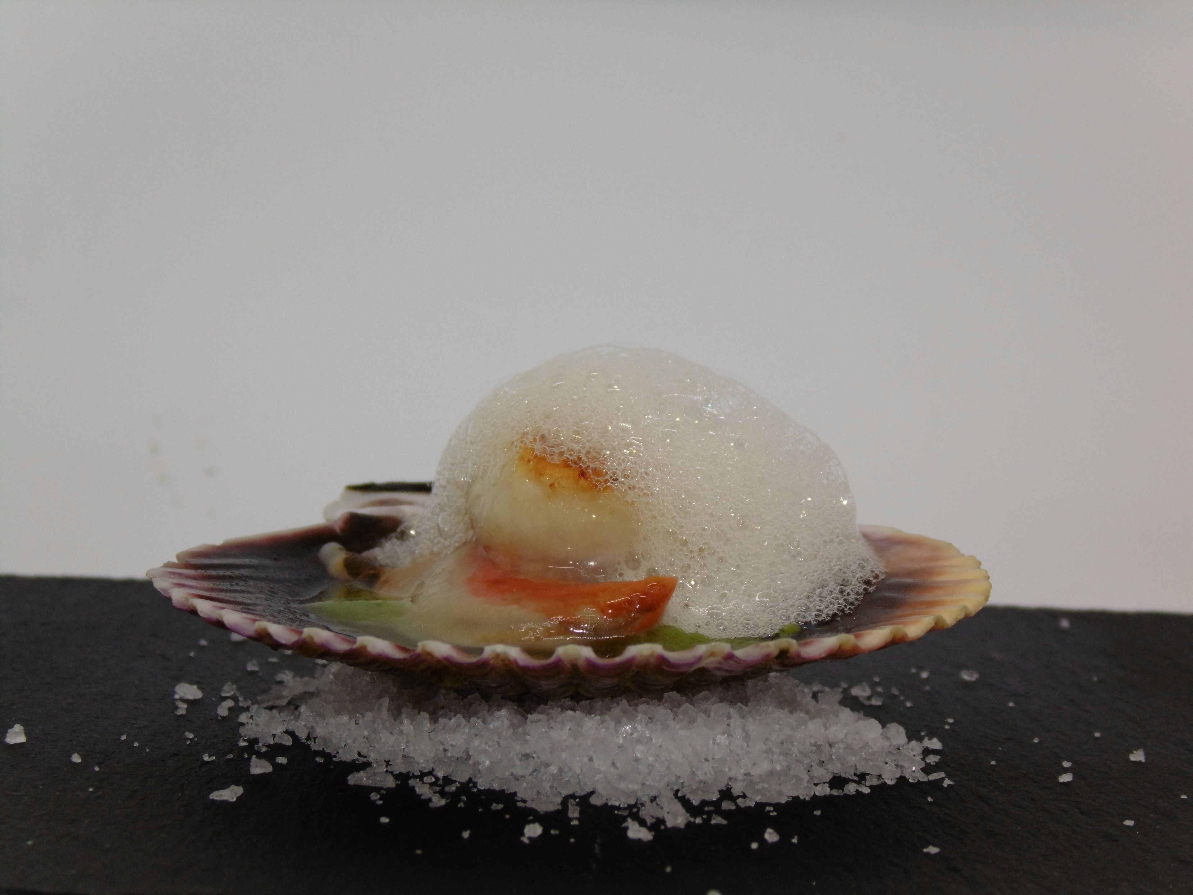 Un dessert servi dans une assiette en forme de coquillage, sur un fond noir.