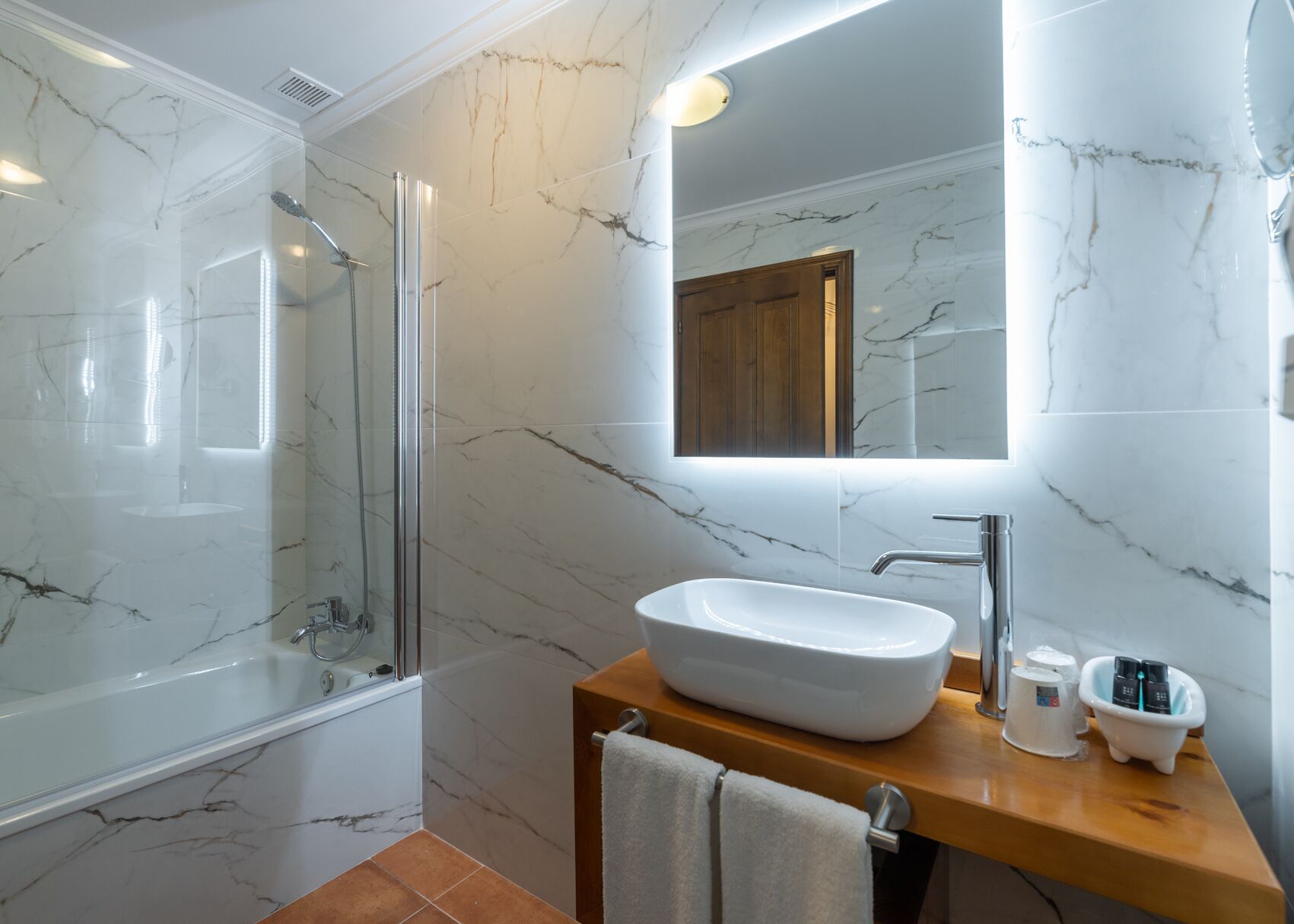 A modern bathroom with a glass-enclosed shower, a wooden vanity with a white sink, and a large mirror.