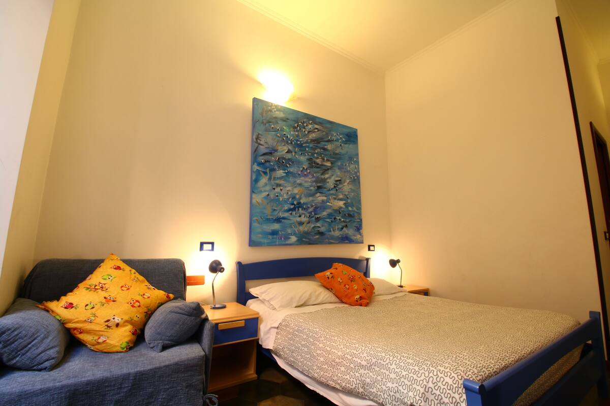 A bedroom with a bed, a chair, a nightstand, and a wall-mounted painting.