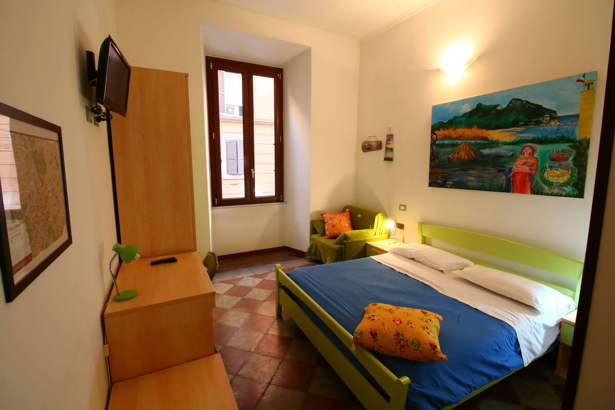 A room with a bed, a desk, a chair, a map on the wall, and a painting.