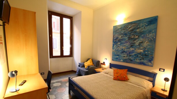 A bedroom with a bed, a desk, a chair, a window, and a painting on the wall. - Trasteverooms La Bernardon (Rome)