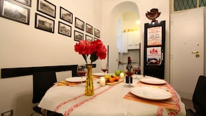 A dining area with a table set for two, featuring a vase with red flowers, a candle, and a fruit platter. - Trasteverooms La Bernardon (Rome)