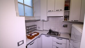 A compact kitchen with white cabinets, a gas stove, and a coffee maker. - Trasteverooms La Bernardon (Rome)