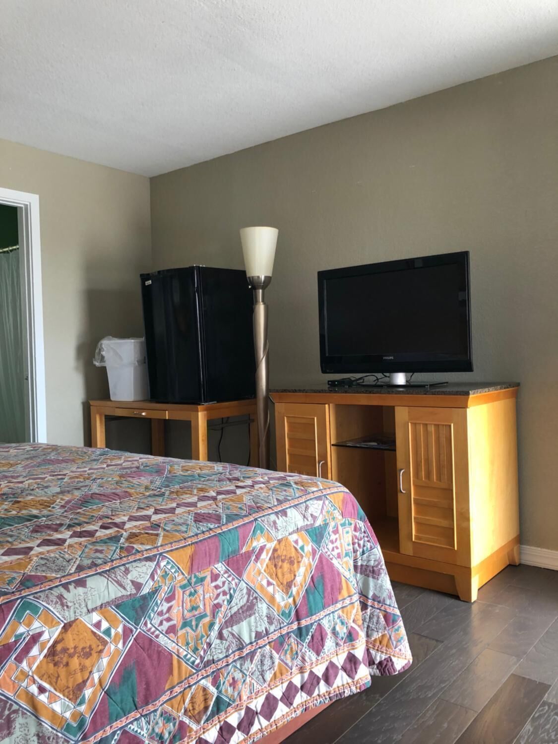 Une chambre d’hôtel avec un lit, un téléviseur posé sur une commode en bois et une lampe sur pied.
