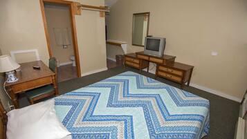 Un dormitorio con cama, escritorio, silla, cómoda, televisor y espejo.