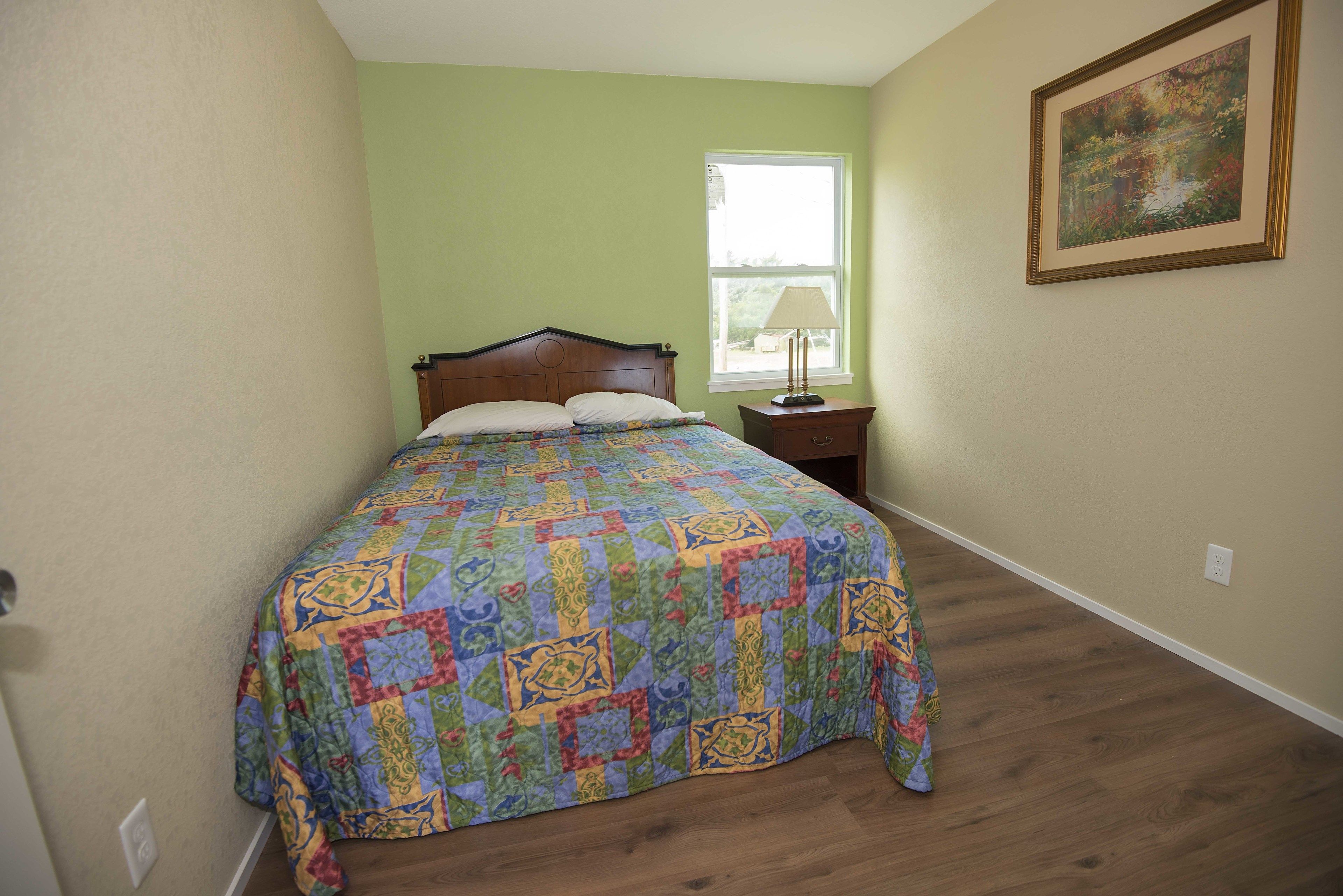 Una camera da letto con un letto in legno, un comodino, una finestra e un quadro appeso al muro.