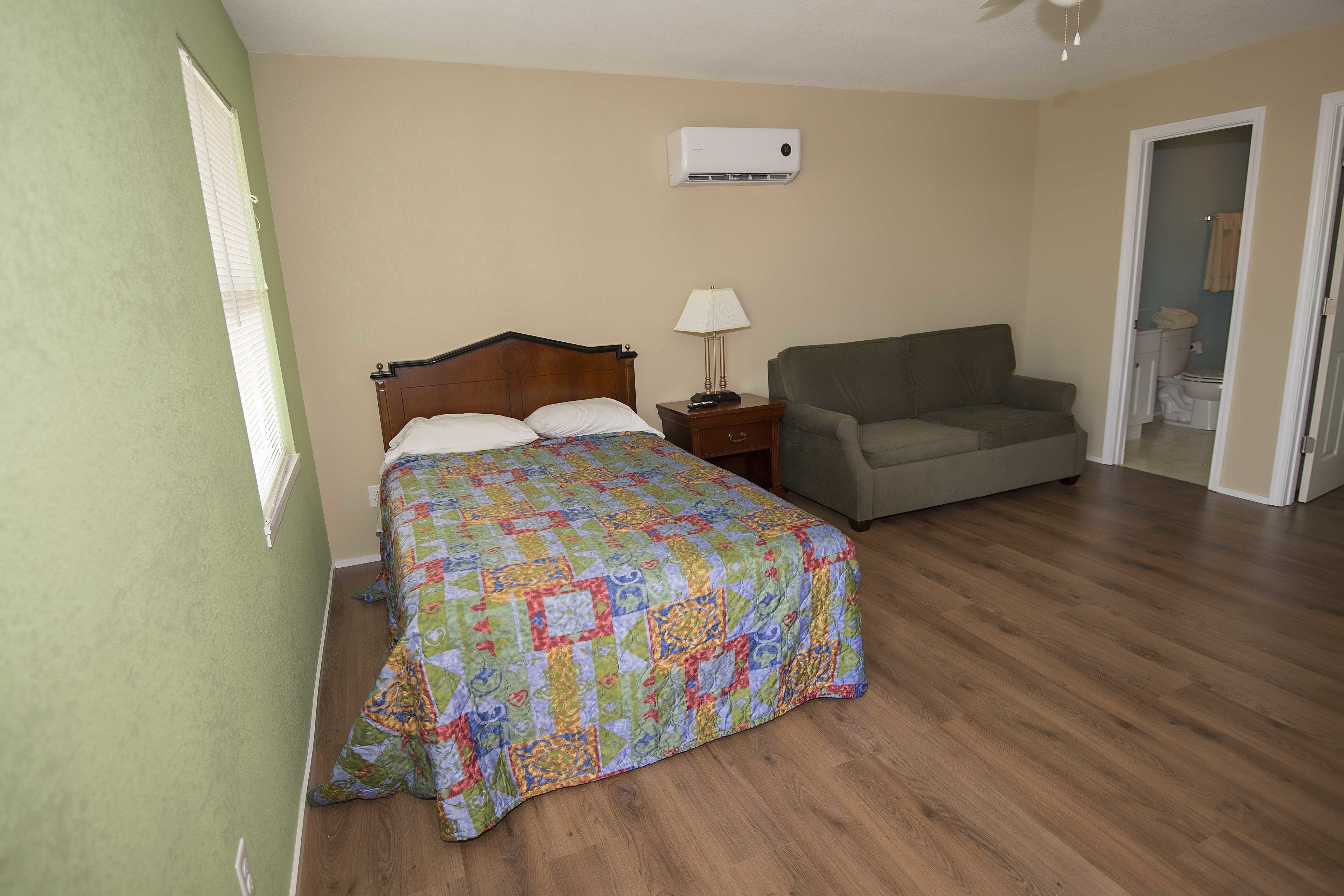 A bedroom with a bed, a nightstand, a lamp, and a sofa.
