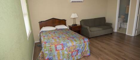 A bedroom with a bed, a nightstand, a lamp, and a sofa.