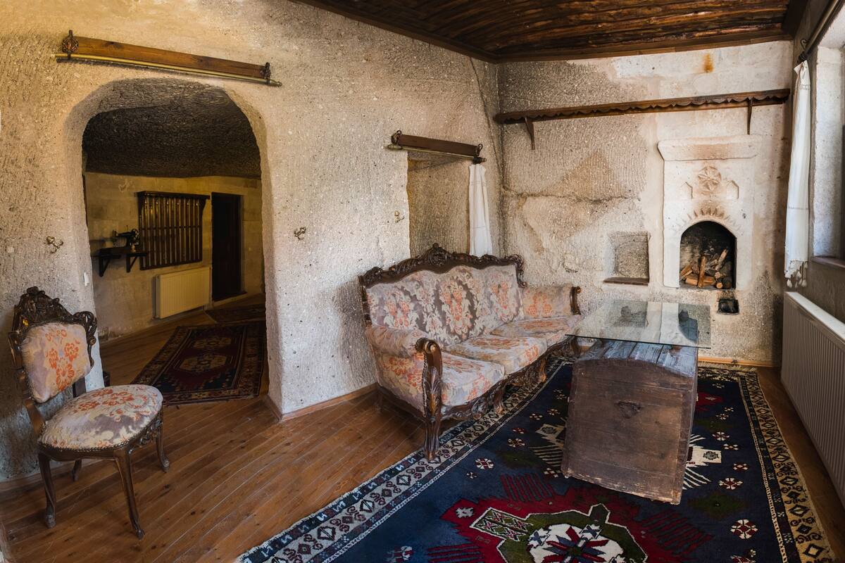 Una habitación tradicional con chimenea, un sofá, suelo de madera y alfombra estampada.