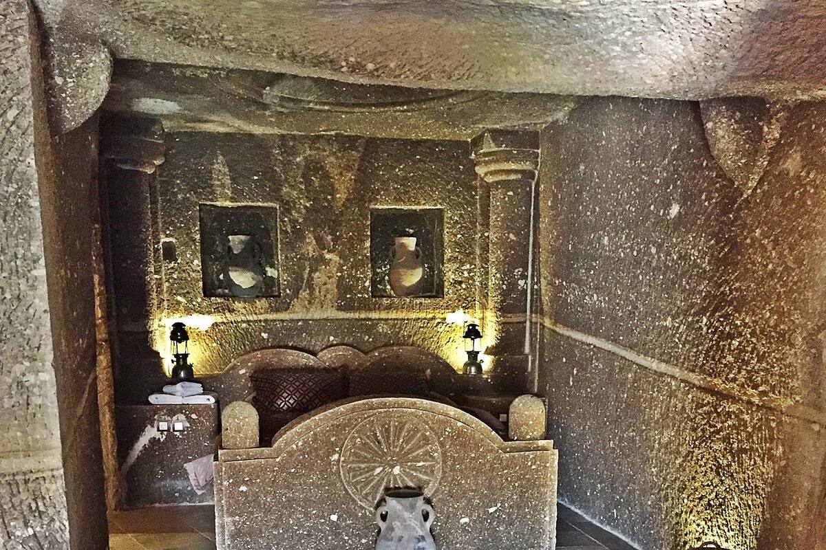 Una habitación con paredes de piedra, una cama, una alfombra y dos lámparas fijadas a la pared.