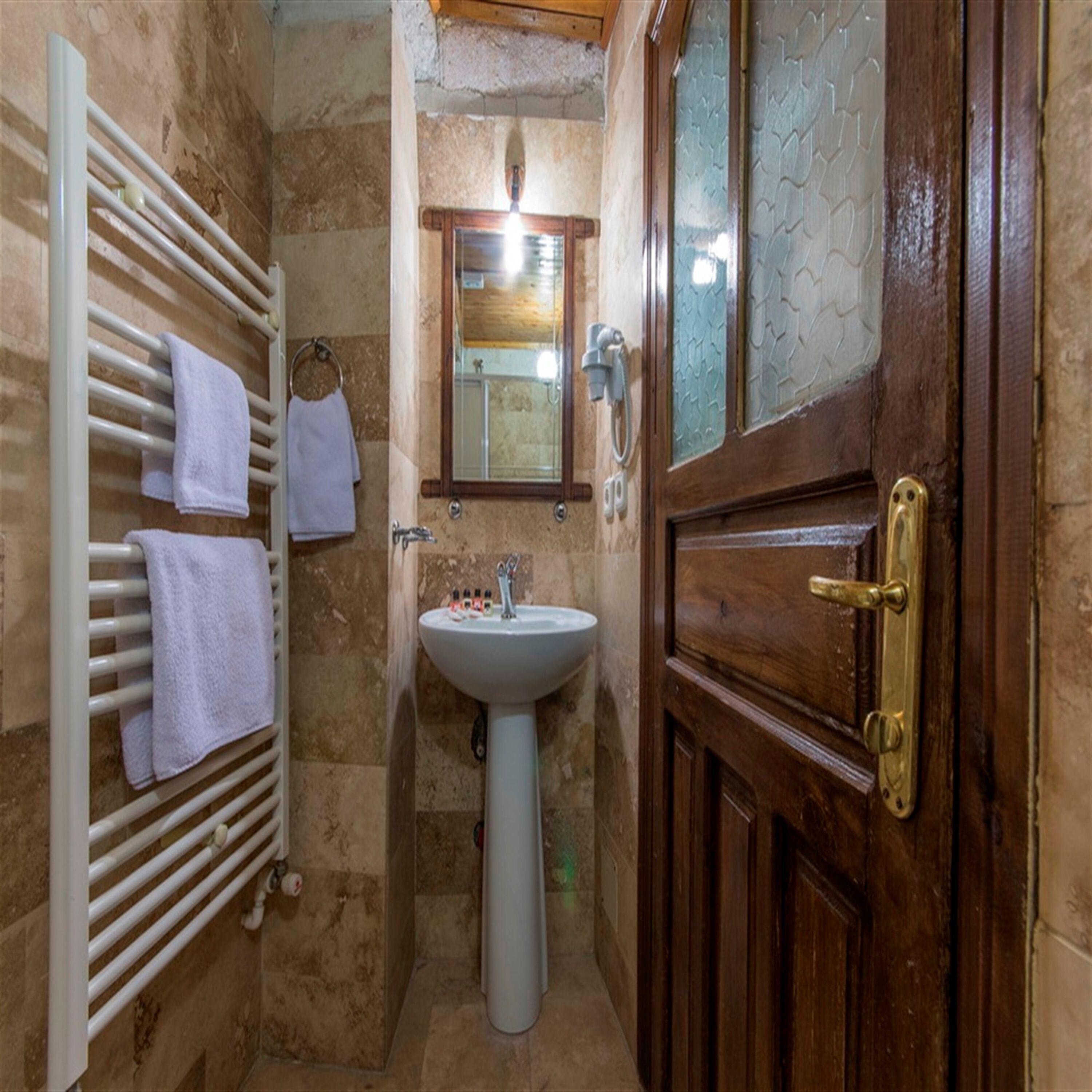 Un baño con puerta de madera, un lavabo blanco y un perchero con toallas.