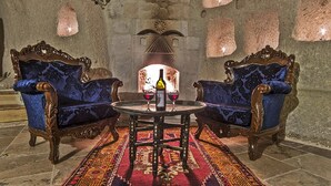 A room with two ornate blue armchairs, a round table with a bottle and glasses, and a patterned rug.